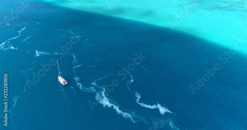 Boat in the Pacific Ocean under the blue sky. We can only see the Ocean and the blue lagoon all over the horizon - aerial view with a drone - travel and vacation concept 