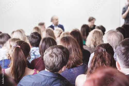 Audience in small classroom. Adult students listen to professor. Group of professionals in audience listening to speaker. Rear view sitting people, business concept. 