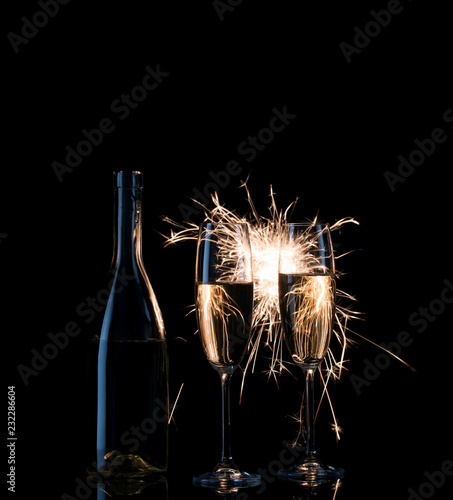 Bottle and two tall glasses of champagne in bright sparks