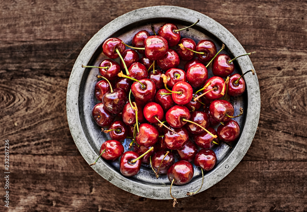 A metallic rustic bowl full of ripe Cherries over a wooden table. A metallic rustic bowl full of ripe Cherries over a wooden table.