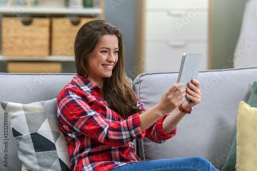 Beautiful young woman on the beige couch at home  holding tablet computer and talking skype
