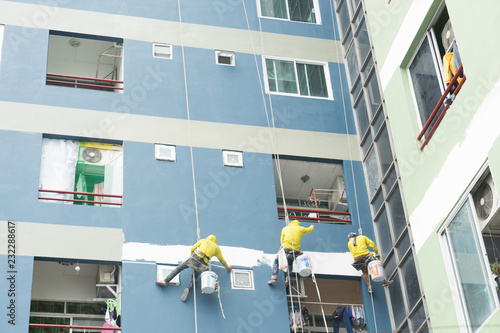 painters hanging on roll, painting color on building wall.