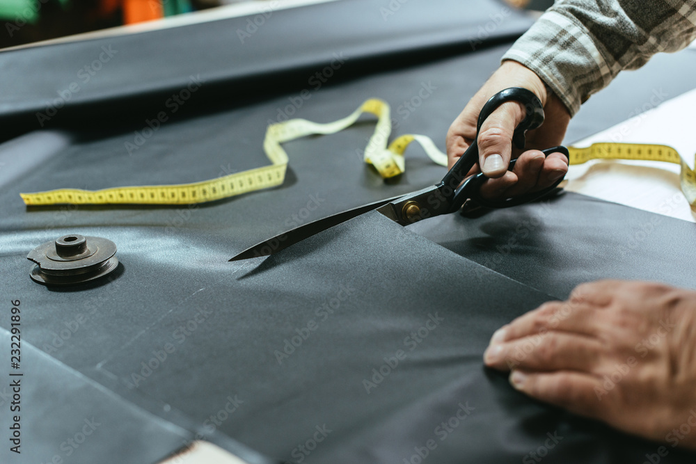 cropped image of male handbag craftsman cutting leather by scissors at workshop