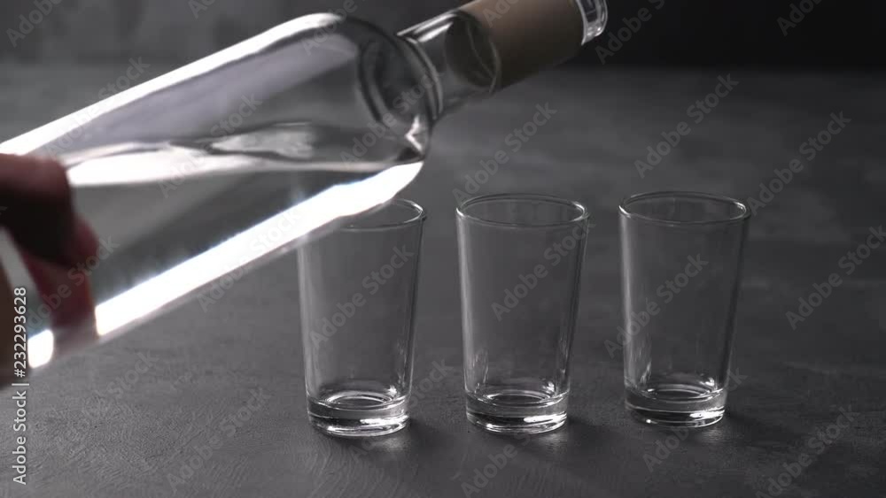 Vodka pouring from a bottle into a glass in a black background. Pouring vodka in glasses close-up. Vodka being poured into a glass Vodka pouring from a bottle into a glass in a black background. Pouring vodka in glasses close-up. Vodka being poured into a glass