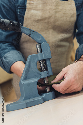 cropped image of male handbag craftsman working with tool at studio