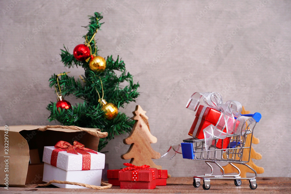 Red gift box on small cart with background gift boxes spill out from paper bag and christmad tree for shopping concept. Red gift box on small cart with background gift boxes spill out from paper bag and christmad tree for shopping concept.