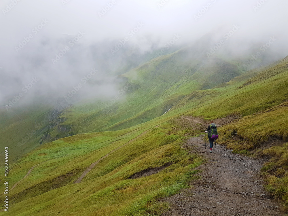 Hiking in cloudy Alps mountains. Woman Traveler with Backpack hiking in the Mountains. mountaineering sport lifestyle concept