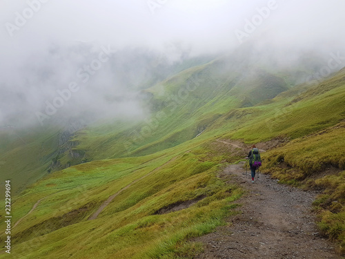 Hiking in cloudy Alps mountains. Woman Traveler with Backpack hiking in the Mountains. mountaineering sport lifestyle concept