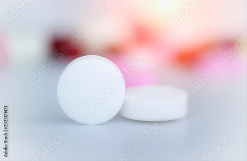 close up white pills with white ground and blurred colorful pills background