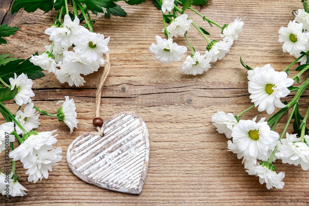 Fototapeta premium Wooden heart among daisy flowers.