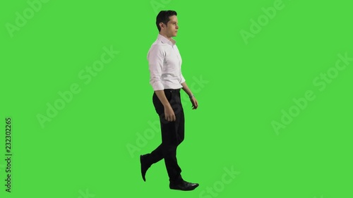 Relaxed young businessman walking and looking around over green screen.