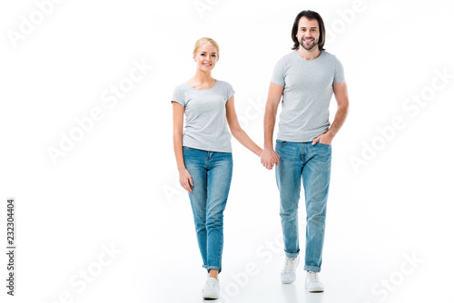 Lovely couple in grey t-shirts holding hands and smiling at camera isolated on white