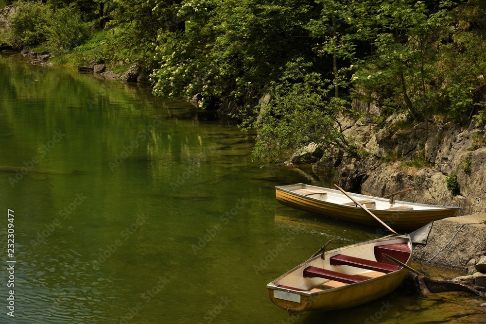 two boats with oars moored to the shore of a mountain lake