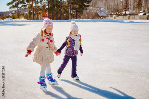 Two little girls hold hands and skate. Space for text.