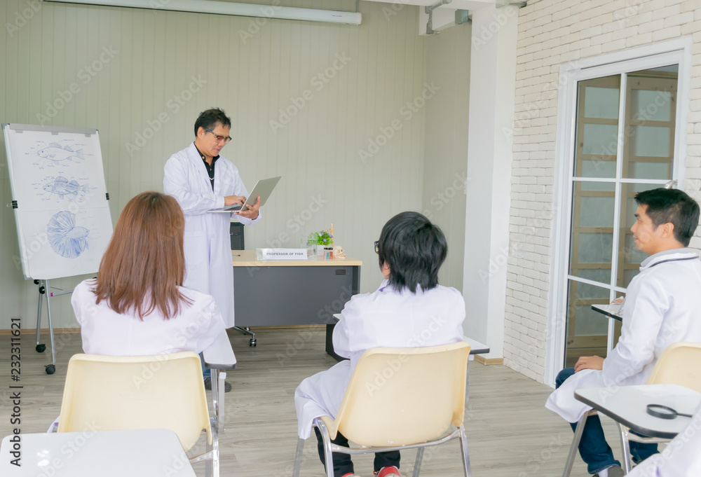 Obraz premium Professor hold the laptop while teaching about the fish anatomy to young scientists and veterinarians doctor. Shooting picture from the back of room. Selective focus.