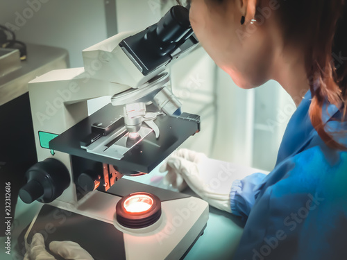 Blurred of scientist being used the microscope to view the appearance of the microbe (bacteria, yeast, mold and fungi) in the microbiological laboratory at the phamaceutical site or university.