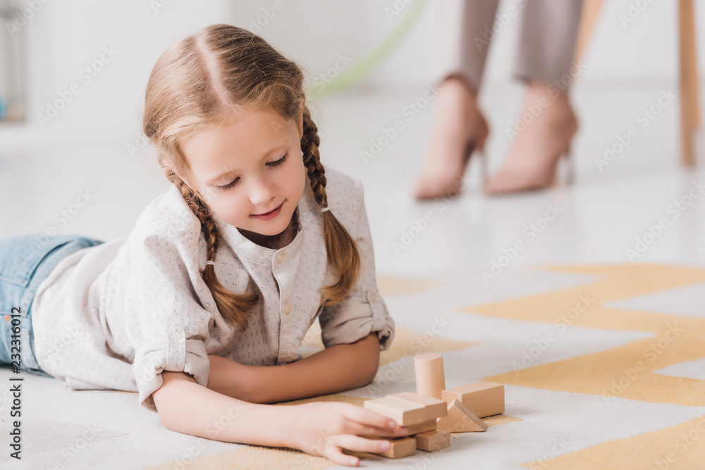 little child playing with wooden blocks on floor with blurred psychologist sitting on background little child playing with wooden blocks on floor with blurred psychologist sitting on background