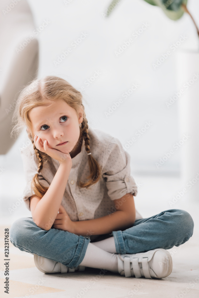thoughtful little child sitting on floor of empty room and looking up thoughtful little child sitting on floor of empty room and looking up