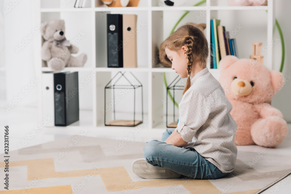 lonely little child sitting on floor in front of shelves with toys lonely little child sitting on floor in front of shelves with toys