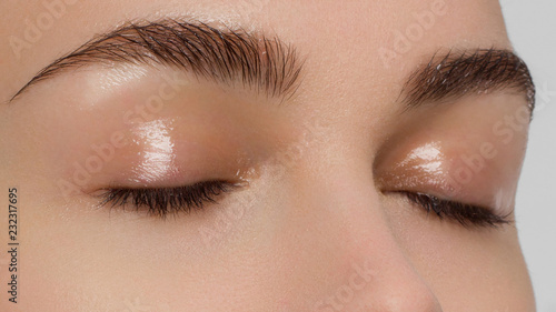 Macro shot of beautiful eyes of the girl with beautiful eyebrows and long eyelashes. One eyebrow is raised. Brown shades in a make-up. Cosmetology, Spa, correction, injections photo