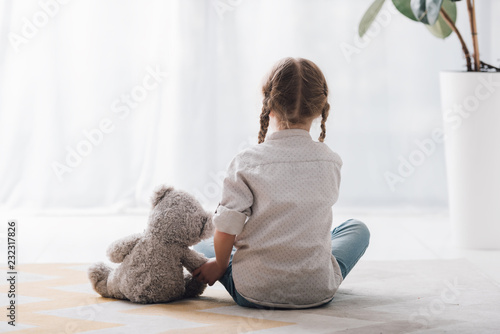rear view of little child sitting on floor with her teddy bear toy