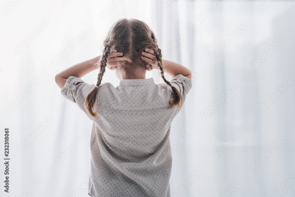 rear view of little child covering ears with hands while standing in ...
