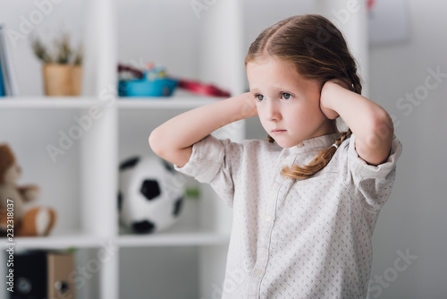 close-up portrait of sad little child covering ears with hands and looking away photo