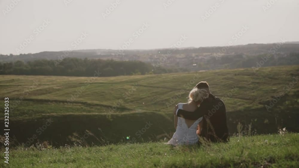 Lovers in a field at sunset,young guy hugging his girlfriend at sunset, sitting on a hill. Lovers in a field at sunset,young guy hugging his girlfriend at sunset, sitting on a hill.