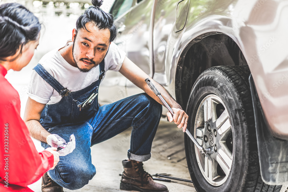 Fixing car engine in automobile repair garage. Handsome mechanics in uniform are repairing car while working in auto service Fixing car engine in automobile repair garage. Handsome mechanics in uniform are repairing car while working in auto service