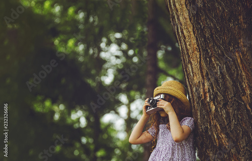 Little girl in straw hat, rustic style dress with retro photo camera in summer park.