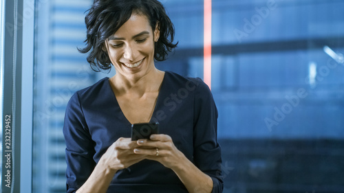 Close-up of the Beautiful Hispanic Woman Using Smartphone. Business Lady in Formal Wear Dress Typing Messages on Mobile Phone. In the Background Window with Cityscape.