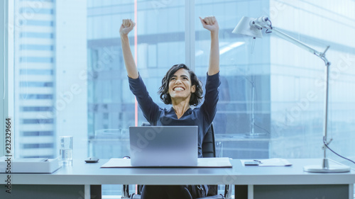 Shot of the Beautiful Businesswoman Sitting at Her Office Desk, Raising Her Arms in a Celebration of a Successful Job Promotion. photo