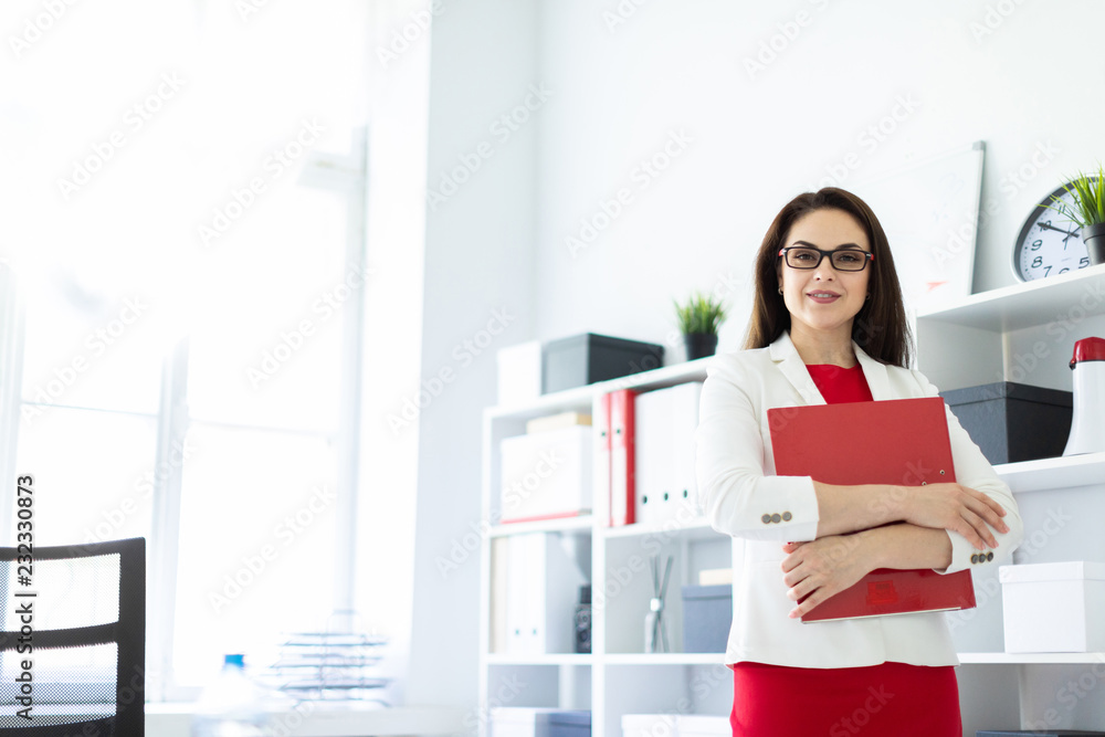 A young girl standing in the office near the table and holding a folder with documents. A young girl standing in the office near the table and holding a folder with documents.