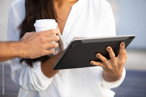 Business partners working at new project on tablet outdoors, cropped shot. Successful businesspeople using digital device and holding coffee cup on meeting. Using gadget concept