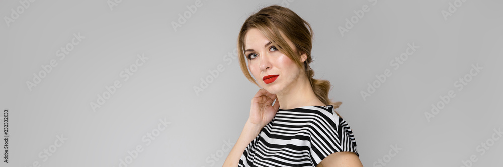 Naklejka premium Attractive young blonde girl in striped blouse serious confident holding her hair standing on gray background