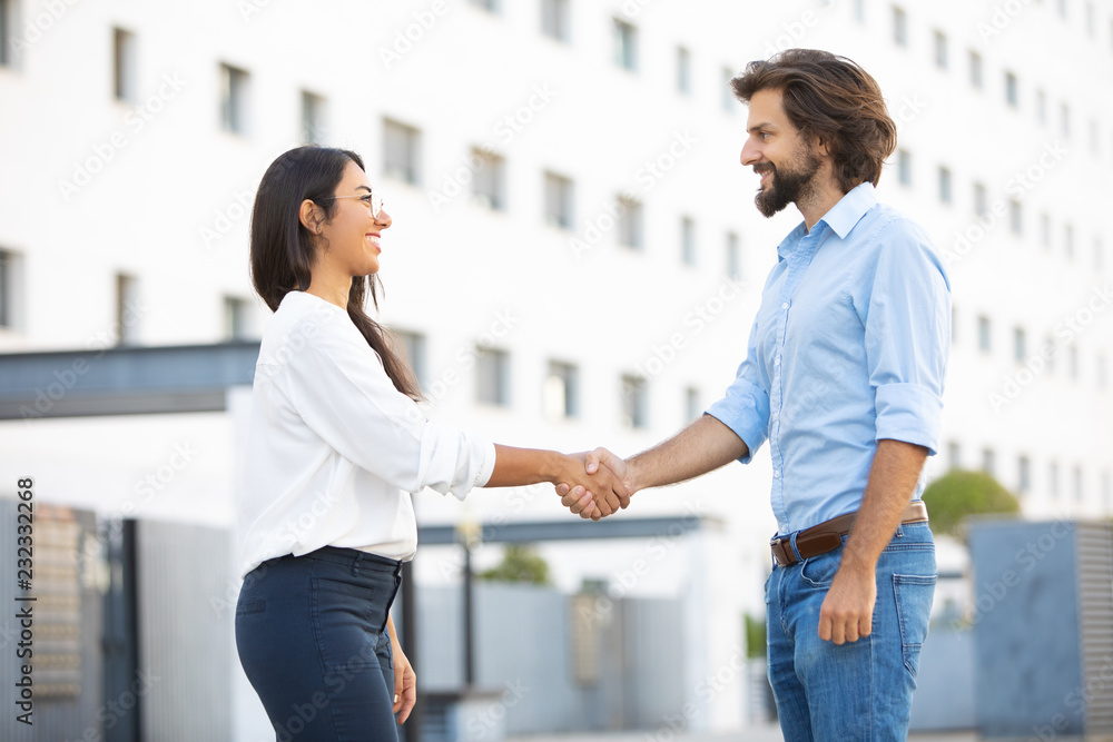 Lucky multicultural partners shaking hands on meeting in city. Professional multiethnic businesspeople near office building, side view. Teamwork concept Lucky multicultural partners shaking hands on meeting in city. Professional multiethnic businesspeople near office building, side view. Teamwork concept