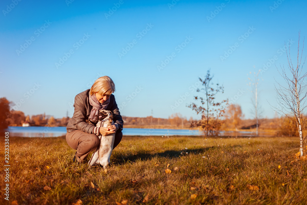Master walking pug dog in autumn park by river. Happy woman hugging pet.