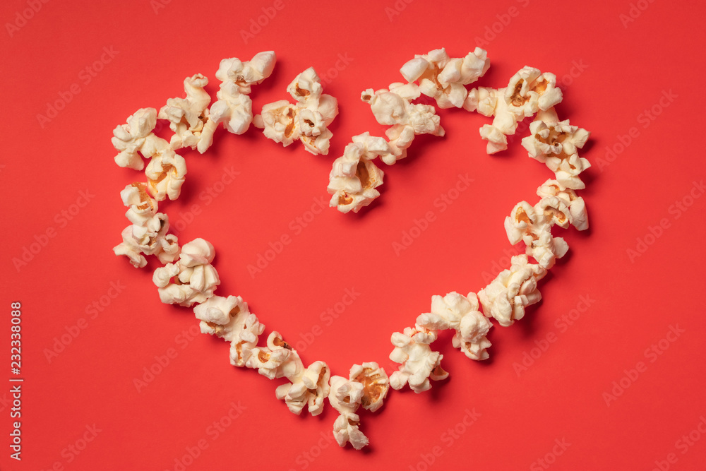 Heart shaped white fluffy popcorn on red background with empty space for text