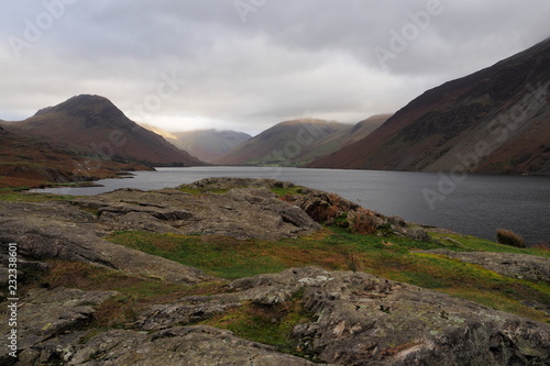Sunlight falls on Great Gable mountain side out of an overcast and cloudy sky set against the dark lake of Wastwater (Wast Water) and scree valley sides, Lake District, Cumbria, UK