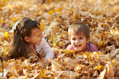 Children are lying and palying in fallen leaves in autumn city park.