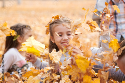 Children are lying and playing on fallen leaves in autumn city park.