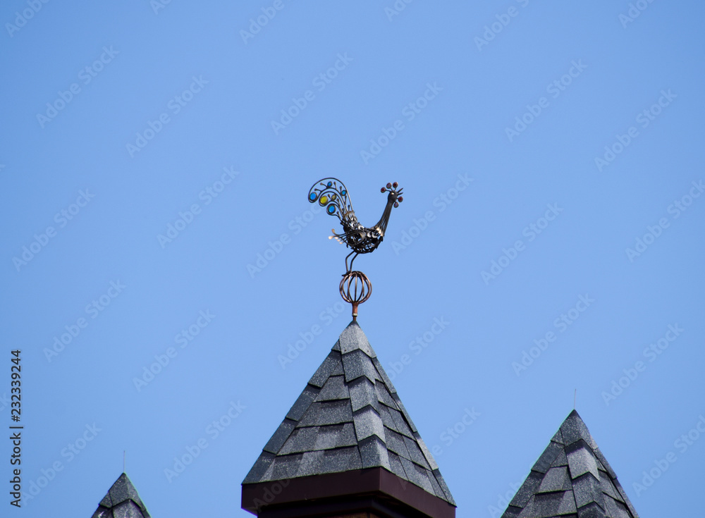 Metal weather vane on top of the building. Weathervane in the form of a singing rooster.