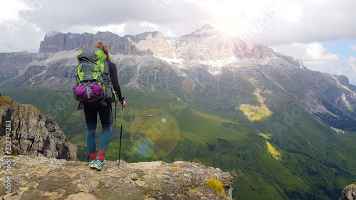 Hiker with backpack relaxing on top of a mountain and enjoying valley view during sunrise