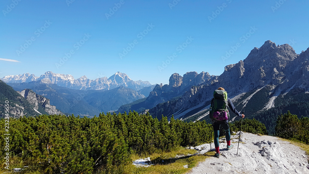 Hiker with backpack relaxing on top of a mountain and enjoying valley view during trip in the alps
