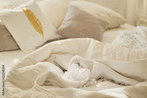 Messy bed. White pillow with blanket on bed unmade. Concept of relaxing after morning. With lighting window. Top view. decorative golden feather on the pillow