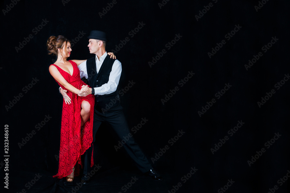 Young beautiful woman in red dress and guy dancing tango on black background in Studio Young beautiful woman in red dress and guy dancing tango on black background in Studio
