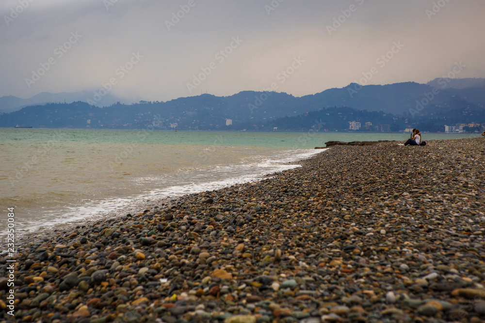 Empty pebble beach of Batumi in cloudy weather. A lonely couple of people on the beach in a storm