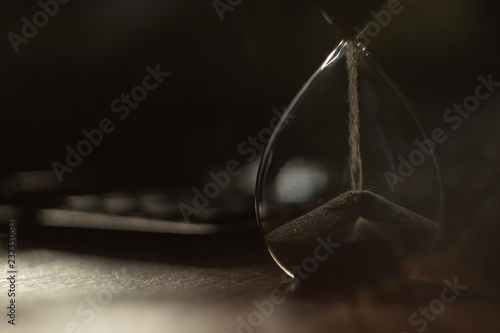 The hourglass is on the table. In the background there is a calculator. The flow of sand is irresistible, like time