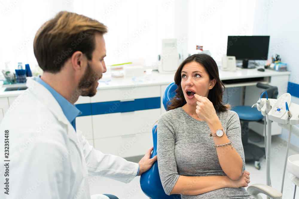 Beautiful woman at the dentist office showing the painful tooth to a beautiful young dentist in the dental clinic. Dentist visit concept.