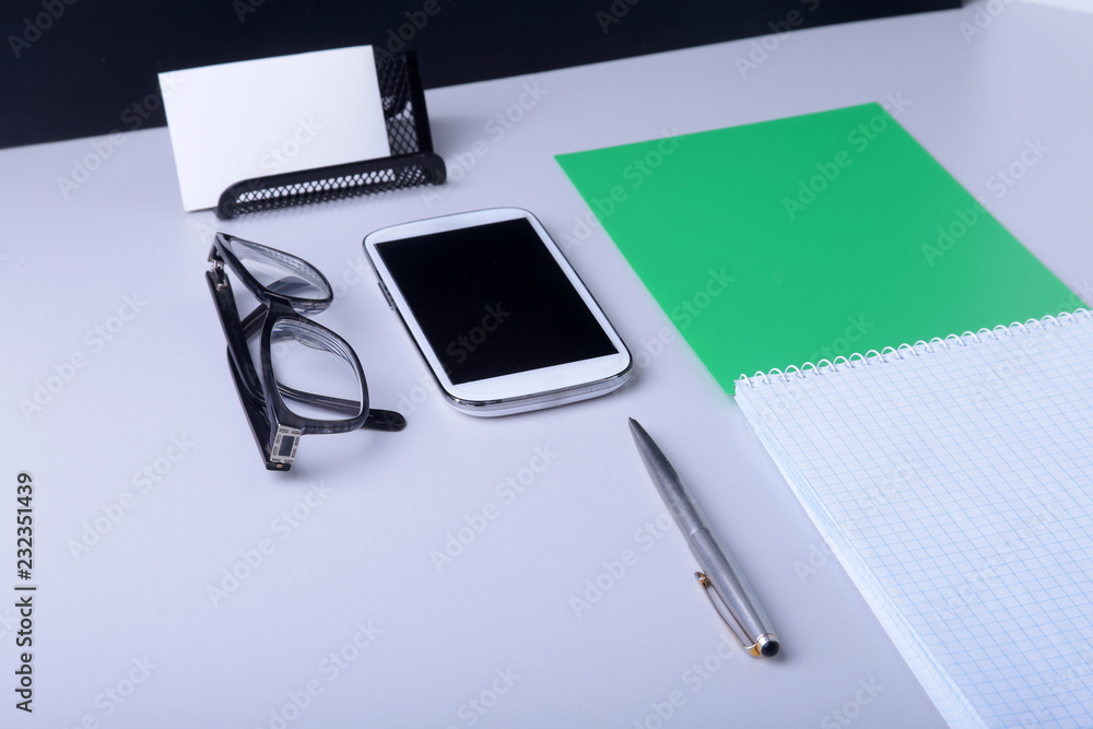 Modern white office desk table with laptop, smartphone and other supplies. Blank notebook page for input the text in the middle. Top view. Modern white office desk table with laptop, smartphone and other supplies. Blank notebook page for input the text in the middle. Top view.